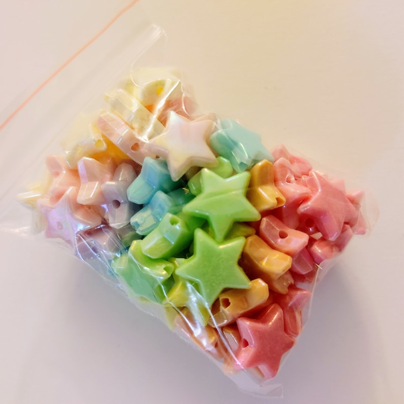 K&ouml;nnte beinhalten: Eine Plastikt&uuml;te gef&uuml;llt mit pastellfarbenen sternf&ouml;rmigen Perlen. Die Perlen sind schimmernd und haben ein Loch in der Mitte zum Auf f&auml;deln.