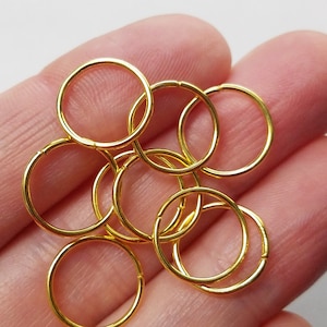 May include: A close-up of a pile of gold jump rings. The rings are all the same size and are arranged in a random pattern.