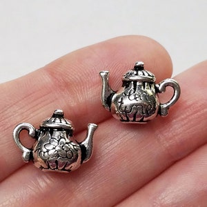 May include: Two silver teapot charm earrings. The teapots have a detailed design with a floral pattern.
