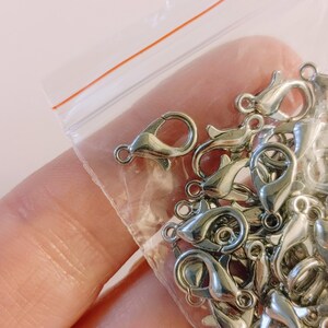 May include: A close-up of a bag of silver-toned lobster clasps. The clasps are small and delicate, and they are perfect for jewelry making.