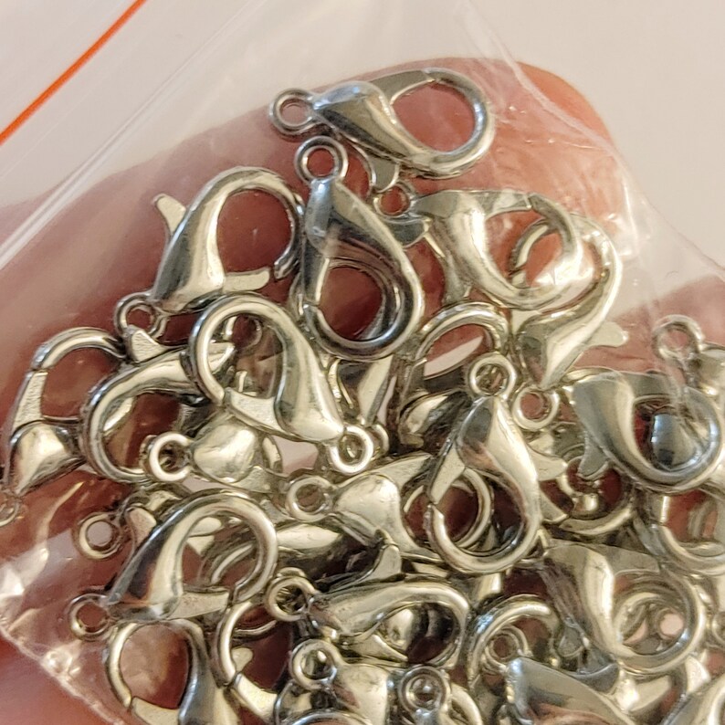 May include: A close-up of a pile of silver-toned lobster clasps. The clasps are small and delicate, and they are perfect for adding a touch of elegance to jewelry.