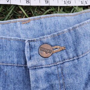 May include: Close-up of a blue denim jean button with a brown metal Wrangler button.