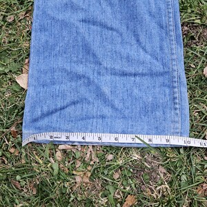May include: A close-up of the bottom of a pair of blue denim jeans with a measuring tape showing the length is 10 inches.