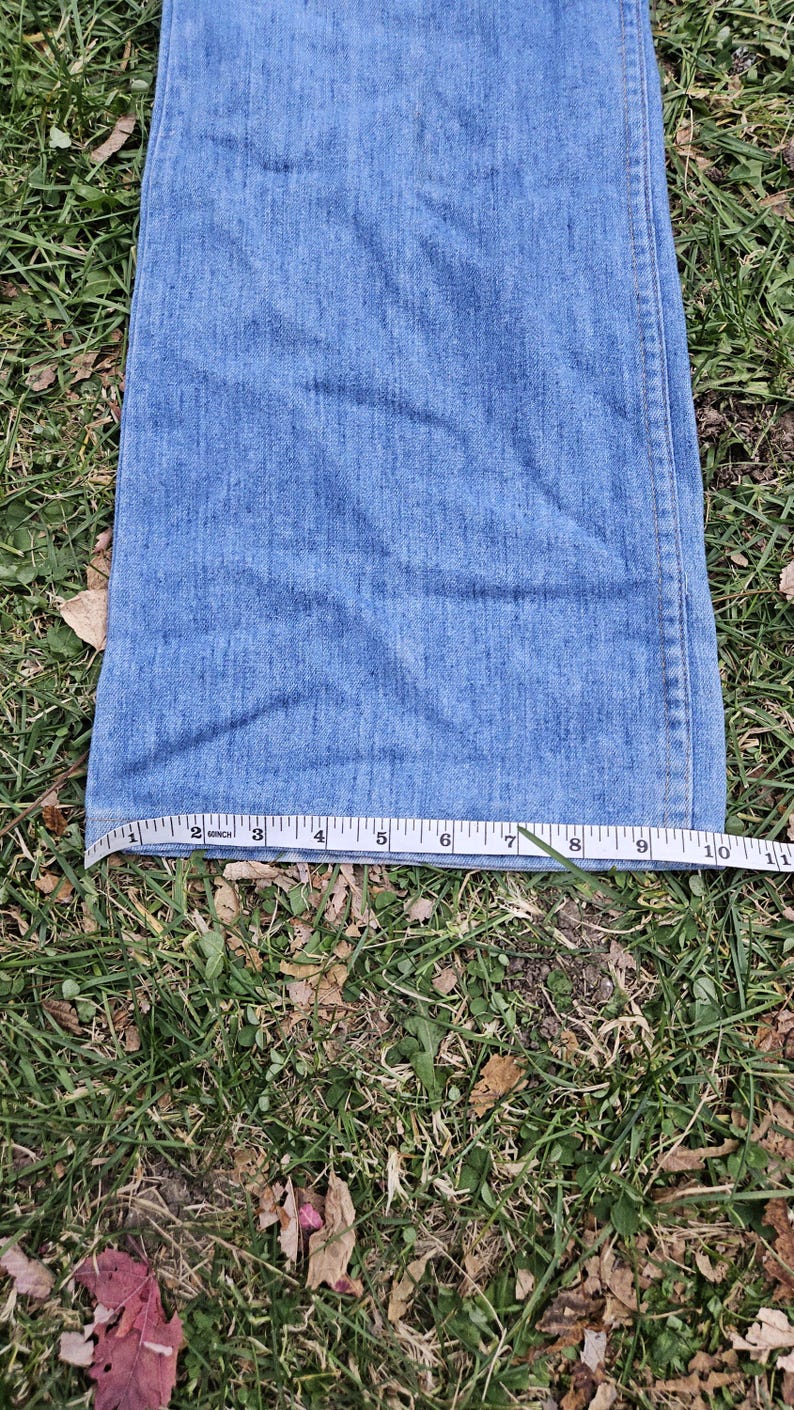 May include: A close-up of the bottom of a pair of blue denim jeans with a measuring tape showing the length is 10 inches.