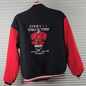 以下が含まれることがあります： 黒と赤のバーシティージャケット。背面には、赤い刺繍で怖い顔をしたカボチャと「Gyro's 3-D World of Terror」の文字が刺繍されている。背面には「ラスベガス、サクラメント、サンノゼ」の文字も刺繍されている。