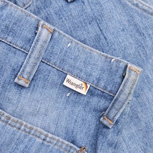 May include: A pair of light blue denim jeans with a brown leather Wrangler label. The jeans have a classic five-pocket style and are folded over.