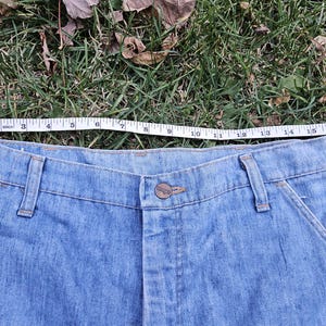 May include: A pair of light blue denim jeans with a button fly and two front pockets. The waist of the jeans is measured with a tape measure, showing a measurement of 38 inches.