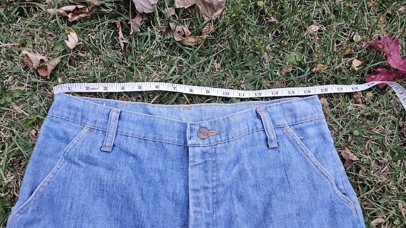 May include: A pair of light blue denim jeans with a button fly and two front pockets. The waist of the jeans is measured with a tape measure, showing a measurement of 38 inches.