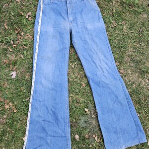 May include: A pair of light blue denim bell bottom pants with a zipper fly and button closure. The pants have a straight leg fit and a wide leg opening.