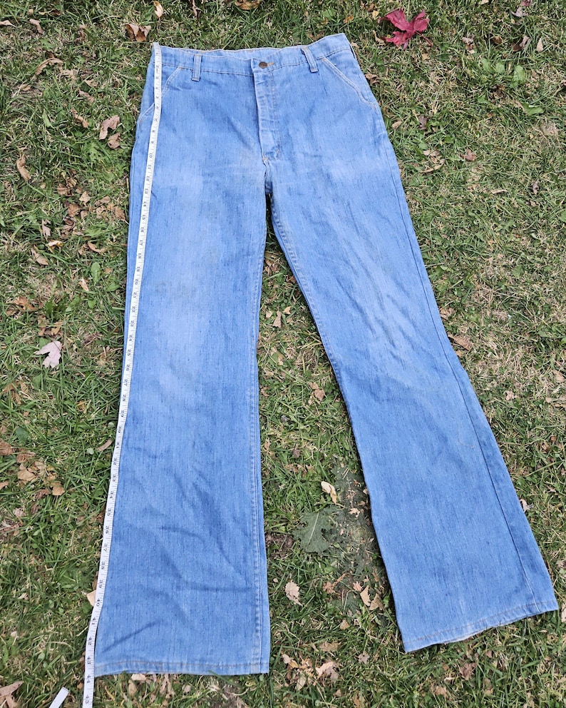 May include: A pair of light blue denim bell bottom pants with a zipper fly and button closure. The pants have a straight leg fit and a wide leg opening.