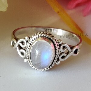 May include: A silver ring featuring a moonstone oval gemstone set in a delicate filigree design. The ring is marked "925" and "omegacrafts" on the band.