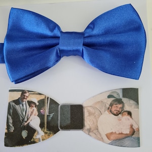 Könnte beinhalten: Ein zweiteiliges Fliegen-Set. Die obere Fliege ist einfarbig königsblau. Die untere Fliege zeigt zwei Vintage-Fotografien, eine von einem Mann und einem Kind und die andere von einem Mann, der ein Baby hält. Der Mittelverbinder ist dunkelgrau.