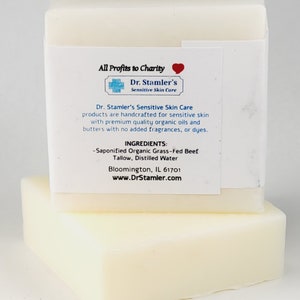 May include: Two bars of white soap stacked on top of each other. The top bar has a label that reads "All Profits to Charity" with a red heart symbol. The label also includes the text "Dr. Stamler's Sensitive Skin Care" and lists the ingredients as "Saponified Organic Grass-Fed Beef Tallow, Distilled Water". The label also includes the website address "www.DrStamler.com".