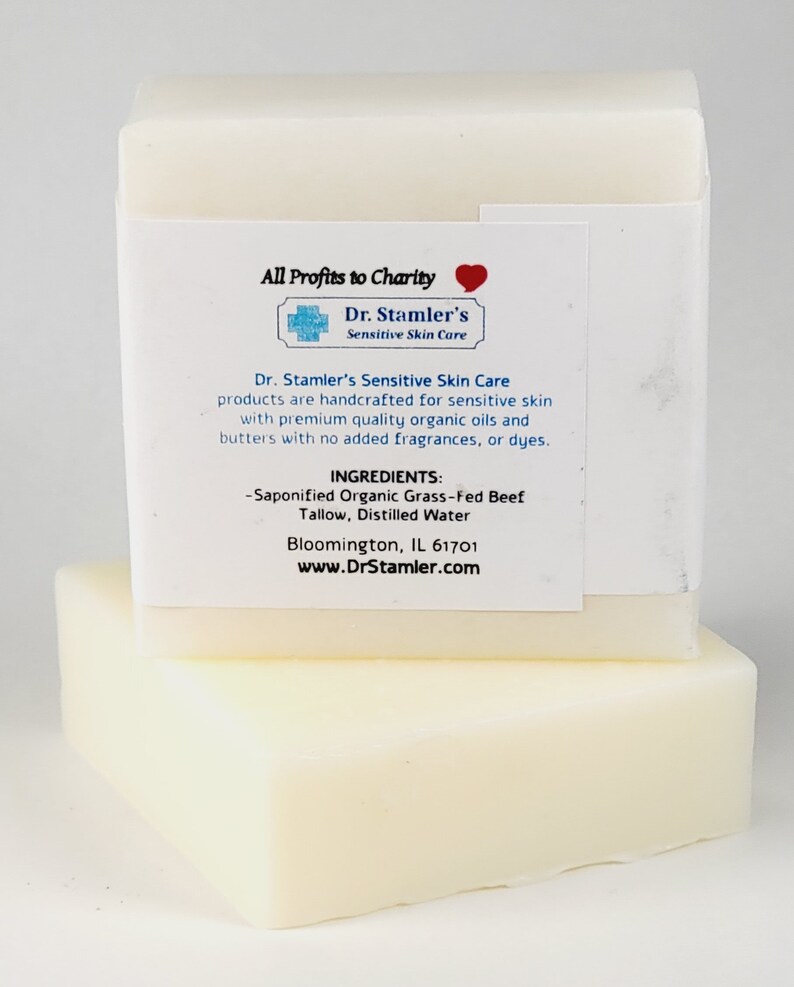 May include: Two bars of white soap stacked on top of each other. The top bar has a label that reads "All Profits to Charity" with a red heart symbol. The label also includes the text "Dr. Stamler's Sensitive Skin Care" and lists the ingredients as "Saponified Organic Grass-Fed Beef Tallow, Distilled Water". The label also includes the website address "www.DrStamler.com".