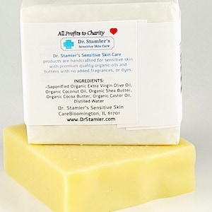 May include: A white bar of soap with a label that reads "All Profits to Charity" and "Dr. Stamler's Sensitive Skin Care". The label lists the ingredients, which include organic extra virgin olive oil, organic coconut oil, organic shea butter, organic cocoa butter, organic castor oil, and distilled water. The soap is handcrafted for sensitive skin and is made with premium quality organic oils and butters. The soap is packaged in a white box.