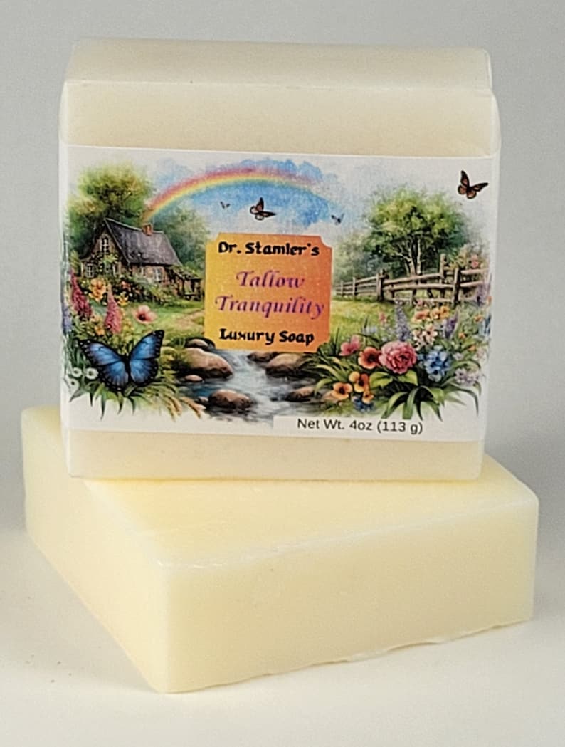 May include: A bar of Dr. Stamler's Tallow Tranquility Luxury Soap, with a net weight of 4 oz (113 g). The soap is wrapped in a white paper with a colorful image of a cottage, a rainbow, butterflies, and flowers.