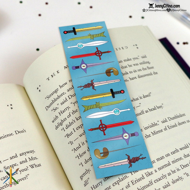 May include: A blue bookmark featuring various cartoon sword designs in yellow, white, red, and green. The bookmark is placed in an open book with text visible on the pages. The bookmark is approximately 2 inches wide and 7 inches long.