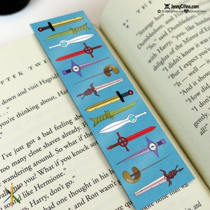 May include: A blue bookmark featuring various cartoon sword designs. The swords are in different colors, including yellow, green, red, and white. The bookmark is placed in a book with text visible. The text "JennyCitino.com" is at the top.
