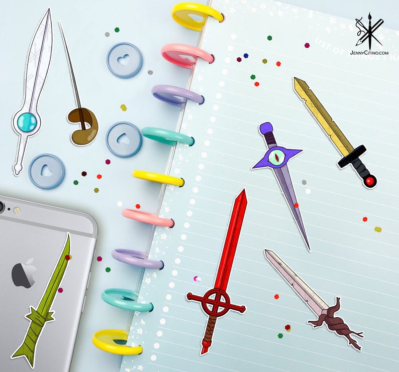 May include: A collection of colorful sword stickers on a blue and white notebook. The stickers feature different styles of swords, including a red sword with a cross, a purple sword with an eye, a yellow sword with a black handle, and a green sword with a brown handle.