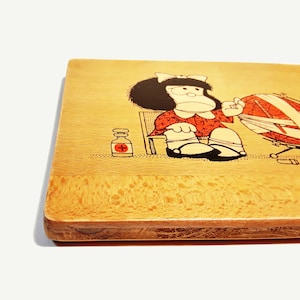 May include: A wooden cutting board with a cartoon illustration of a girl with black hair and a red dress. She is sitting in a chair and holding a ball of yarn. There is a bottle of medicine next to her.