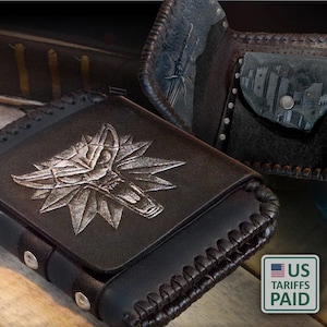 Puede incluir: Cartera de cuero negro con un emblema de cabeza de lobo plateado. La cartera abierta revela un interior detallado con un bolsillo para monedas y ranuras para tarjetas. El diseño incluye un borde cosido y una ilustración de paisaje.