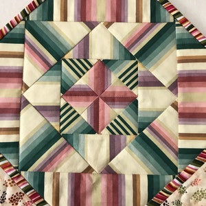 Peut inclure: Gros plan sur un bloc de courtepointe avec un motif g&eacute;om&eacute;trique de rayures dans les tons de rose, vert et marron. Le bloc de courtepointe est compos&eacute; de carr&eacute;s de tissu cousus ensemble pour cr&eacute;er un motif en forme d'&eacute;toile.