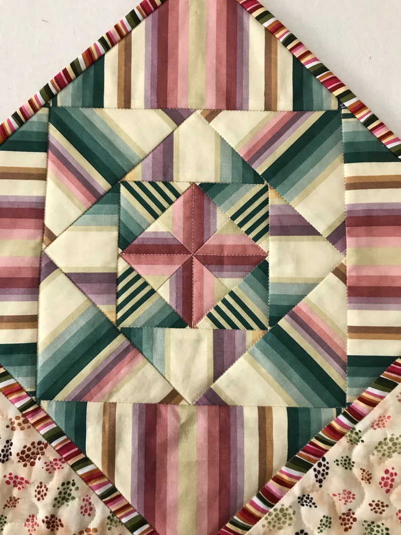 Peut inclure: Gros plan sur un bloc de courtepointe avec un motif g&eacute;om&eacute;trique de rayures dans les tons de rose, vert et marron. Le bloc de courtepointe est compos&eacute; de carr&eacute;s de tissu cousus ensemble pour cr&eacute;er un motif en forme d'&eacute;toile.