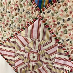 Peut inclure: Une courtepointe en patchwork avec un motif g&eacute;om&eacute;trique au centre. La courtepointe est faite de diff&eacute;rents tissus, y compris des motifs ray&eacute;s, floraux et &agrave; pois. Les couleurs sont le rose, le brun, le blanc et le bleu.