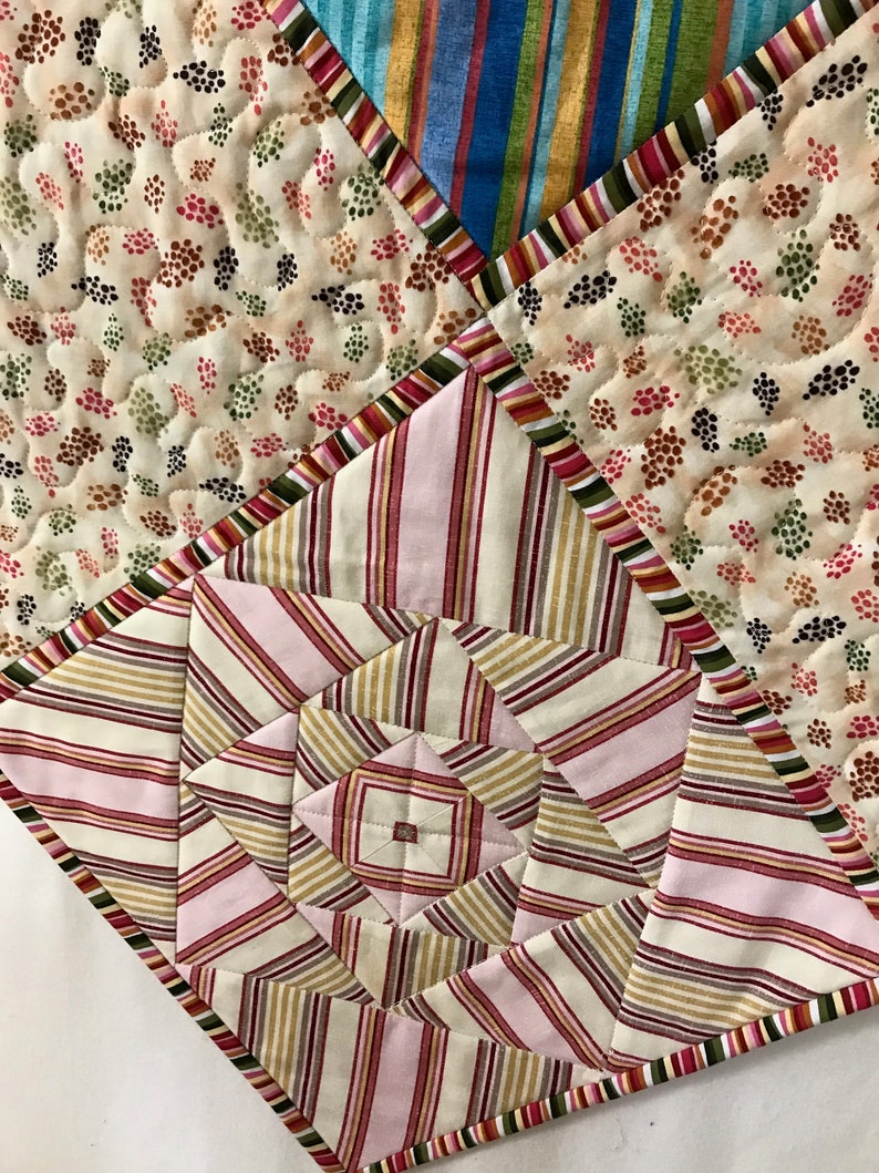 Peut inclure: Une courtepointe en patchwork avec un motif g&eacute;om&eacute;trique au centre. La courtepointe est faite de diff&eacute;rents tissus, y compris des motifs ray&eacute;s, floraux et &agrave; pois. Les couleurs sont le rose, le brun, le blanc et le bleu.