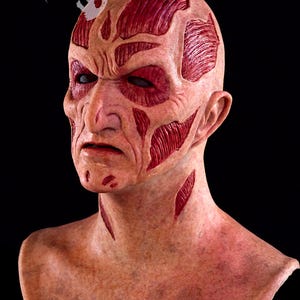 May include: A detailed, realistic mask depicting a scarred face with exposed muscle tissue. The mask features a pale complexion with deep red lacerations and exposed muscle. The eyes are dark and sunken. The Moonstruck Studios logo is visible.