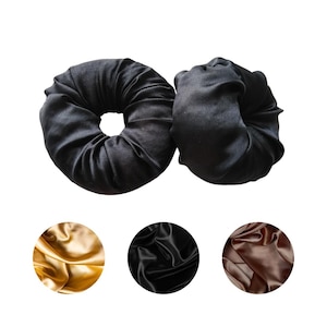 May include: Two black satin hair bun makers. The bun makers are round and have a hole in the center. Below are three swatches of fabric in gold, black, and brown.