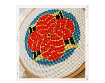 May include: A red, yellow, and blue cross-stitch design of a stylized flower in a circular wooden embroidery hoop.