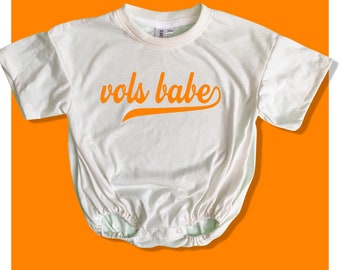 May include: A white baby onesie with an orange graphic that says "vols babe" in a retro font.