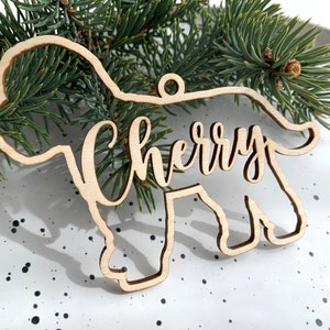 Può includere: Un ornamento natalizio in legno a forma di cane con il nome "Cherry" scritto in corsivo sul corpo.