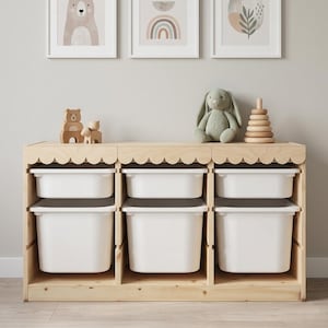 May include: A wooden toy storage unit with six white bins. The unit has a scalloped edge and is topped with a plush bunny, a wooden stacking toy, and wooden bear figurines. Three framed art pieces hang above.
