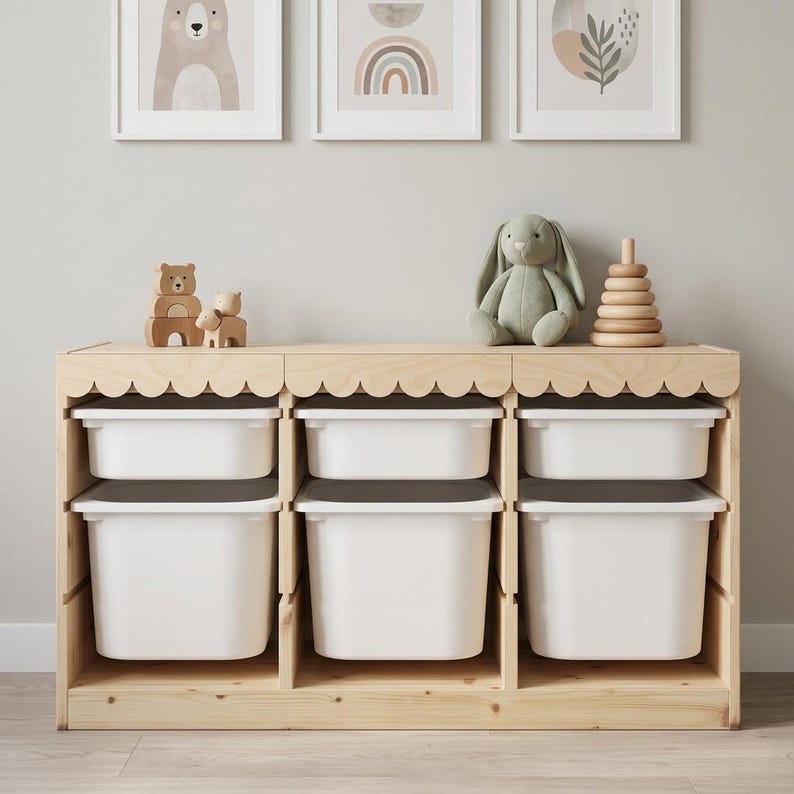 May include: A wooden toy storage unit with six white bins. The unit has a scalloped edge and is topped with a plush bunny, a wooden stacking toy, and wooden bear figurines. Three framed art pieces hang above.