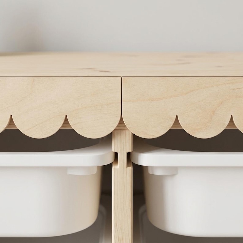 May include: A light-colored wooden storage unit with a scalloped edge design. The unit has two white storage bins visible below. The wood has a natural finish, and the bins are a solid white color. The design is simple and modern.