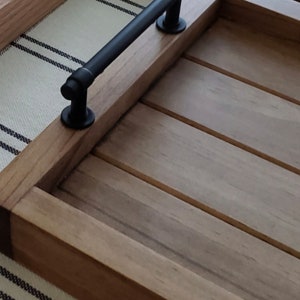 May include: A wooden serving tray with a black metal handle. The tray has a natural wood finish and is made of solid wood.