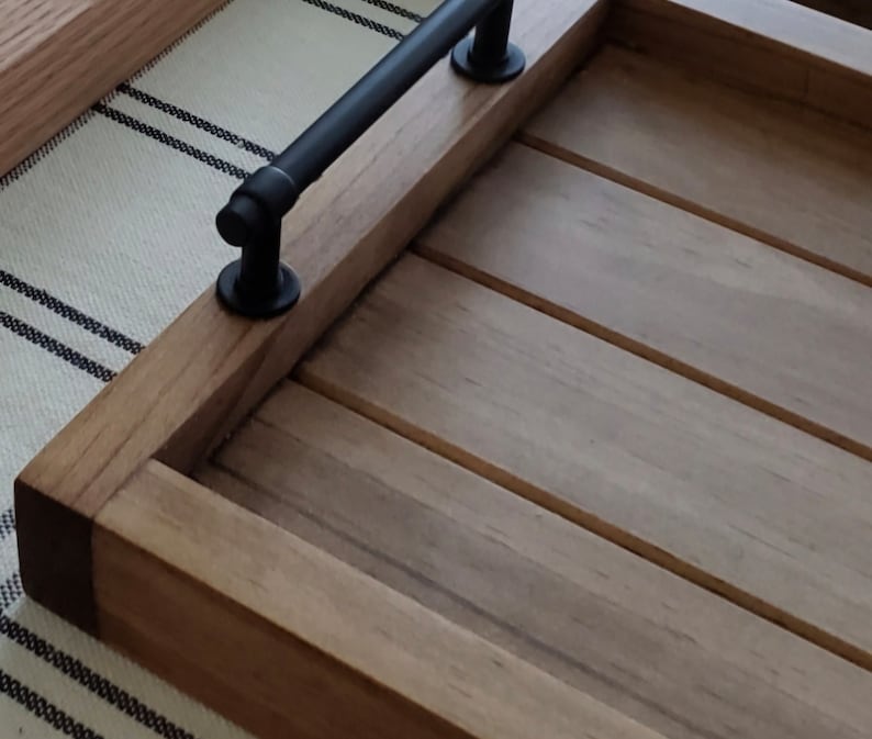 May include: A wooden serving tray with a black metal handle. The tray has a natural wood finish and is made of solid wood.