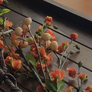 May include: A close-up of a floral arrangement with orange and white flowers and green leaves. The flowers are arranged on a wooden surface.