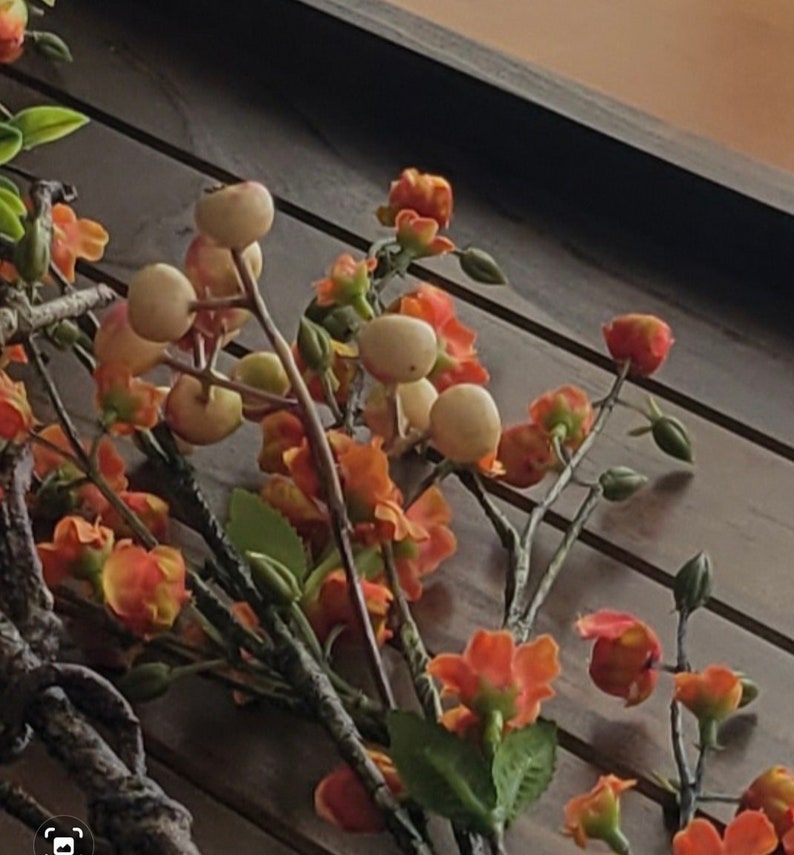 May include: A close-up of a floral arrangement with orange and white flowers and green leaves. The flowers are arranged on a wooden surface.