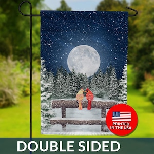 May include: Double-sided garden flag featuring a winter scene with two cardinals perched on a snowy bench. The background shows a full moon, falling snow, and snow-covered pine trees. The flag is printed in the USA.