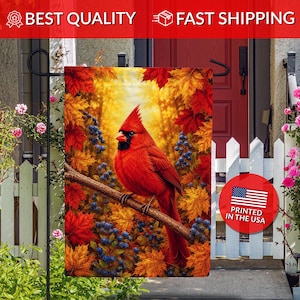 May include: A rectangular garden flag featuring a vibrant red cardinal perched on a tree branch. The background displays a dense forest of autumn maple leaves in shades of orange, yellow, and red, accented by clusters of dark blue berries.