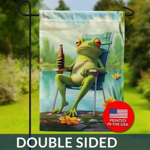 May include: Double-sided garden flag featuring a cartoon frog relaxing in a chair by a lake, holding a bottle of beer. The frog is green with orange eyes. The flag has the text "DOUBLE SIDED" and "PRINTED IN THE USA".