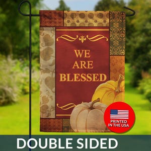 May include: Double-sided garden flag with a fall theme. The flag features the text "WE ARE BLESSED" on a burgundy background, with pumpkins and decorative borders. The flag is printed in the USA.