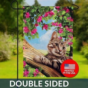May include: Double-sided garden flag featuring a tabby cat resting on a tree branch, surrounded by pink flowers and green foliage. The flag has the text "DOUBLE SIDED" at the bottom and a "PRINTED IN THE USA" logo.