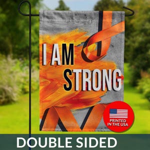 May include: Double-sided garden flag with the words "I AM STRONG" in white lettering. The flag features an orange ribbon and brushstroke design on a gray background. A red circle with the American flag and "PRINTED IN THE USA" is visible.