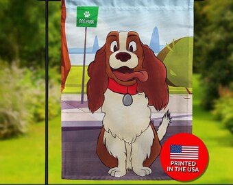 May include: Double-sided garden flag featuring a cartoon dog with brown and white fur, a red collar, and a long tongue. The flag has a light blue sky background and a green "Dog Park" sign. The flag is printed in the USA.