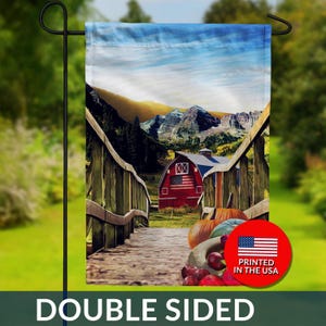 May include: Double-sided garden flag featuring a rustic barn scene with a red barn, wooden bridge, and pumpkins. The barn has an American flag design. The flag is printed in the USA.