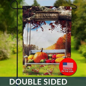May include: Double-sided garden flag featuring a fall scene with a wooden swing, pumpkins, and apples. The flag has the word "Blessings" on a wooden sign and a red circle with "Printed in the USA".